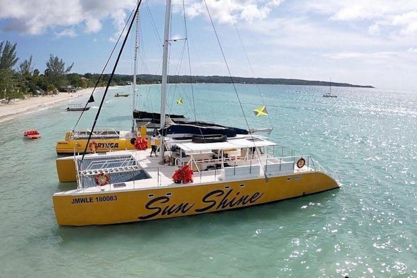 A yellow catamaran named 'Sun Shine' with the registration number 'JMWLE 180083' on a calm sea with a beach in the background. 4