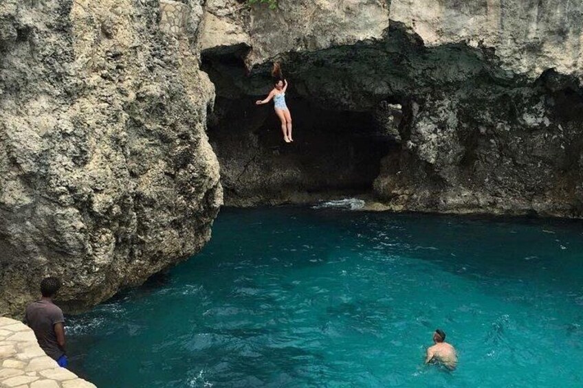 A person jumping from a cliff into a pool, another person swimming, and a third person standing by the pool. 2