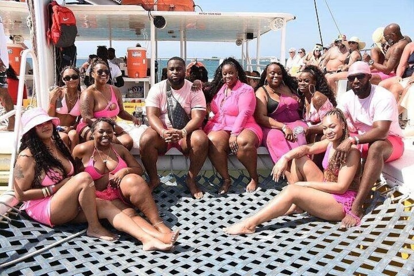 A group of people on a boat with a metal lattice floor, wearing pink and white clothing, and a clear sky in the background. 3