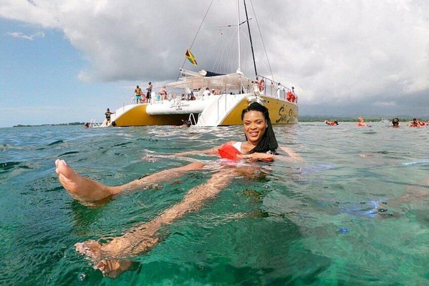 A person floating in clear turquoise water with a boat in the background. 4