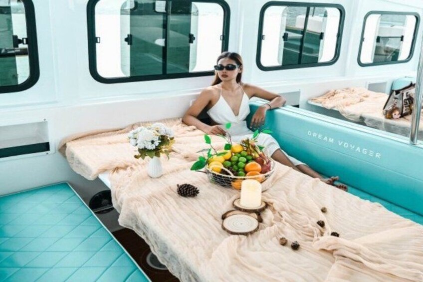A woman sitting on a bed with a table full of fruits and flowers. 2