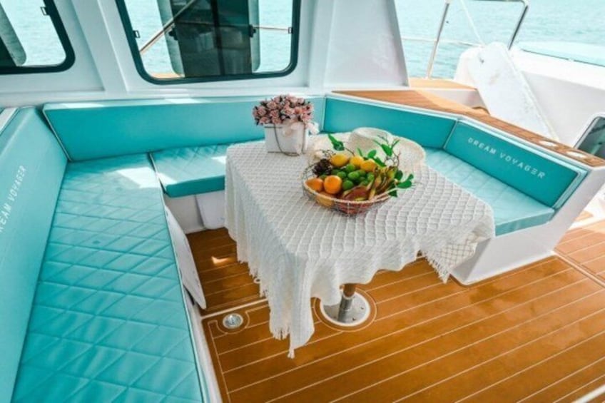 L’intérieur d’un bateau, avec des coussins de couleur turquoise, une table recouverte d’une nappe tissée et un panier de fruits. 4