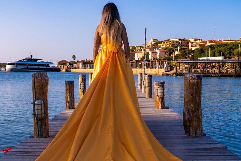 A woman in a yellow dress standing on a wooden pier with a boat in the background. 4