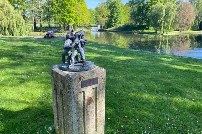 A statue of soldiers on a pedestal by a lake in a park. 1