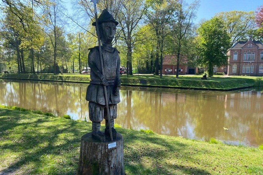 A statue of a historical figure in a park with a pond and buildings in the background. 3