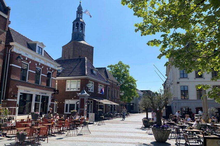 A street with outdoor seating, buildings, and a church tower. 5