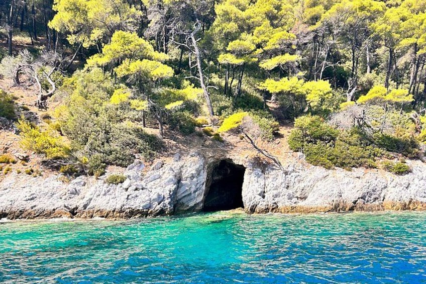A coastal landscape with a rocky cave entrance, clear turquoise waters, and dense green vegetation. 4