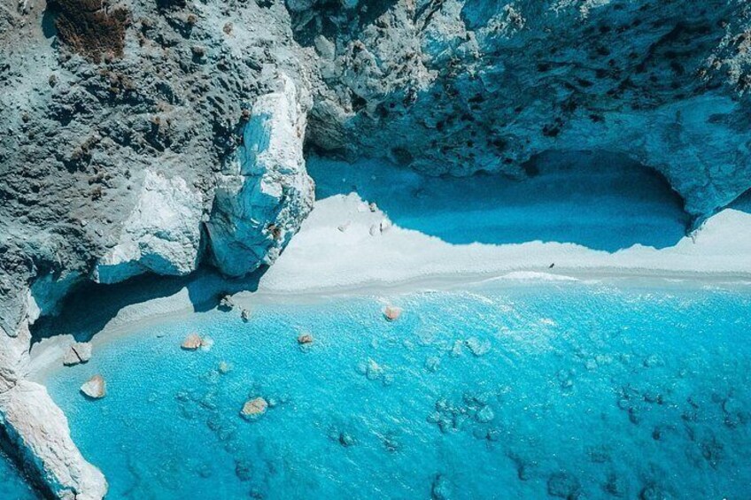 Ein türkisfarbener Strand mit weißem Sand und klarem, blauem Wasser, umgeben von felsigen Klippen. 2