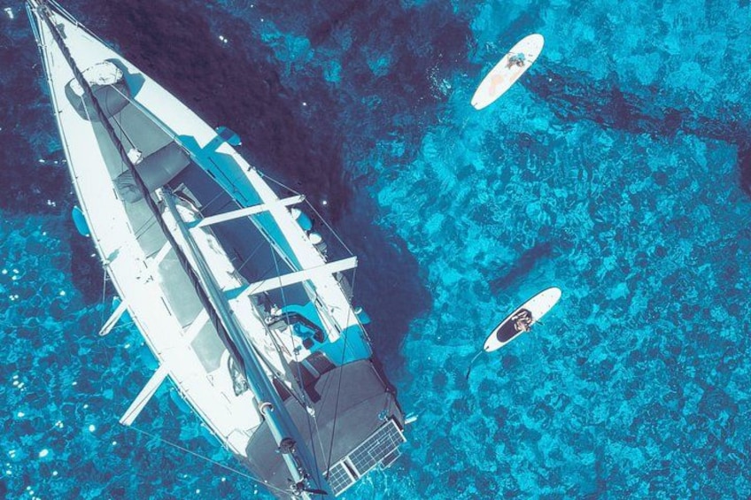 A sailboat with two smaller boats nearby in clear blue water. 1