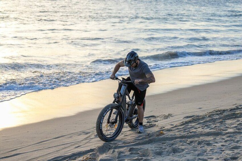 A person riding a bicycle on a sandy beach with waves in the background. 1
