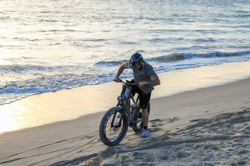 Une personne fait du vélo sur une plage de sable, avec des vagues en arrière-plan. 1