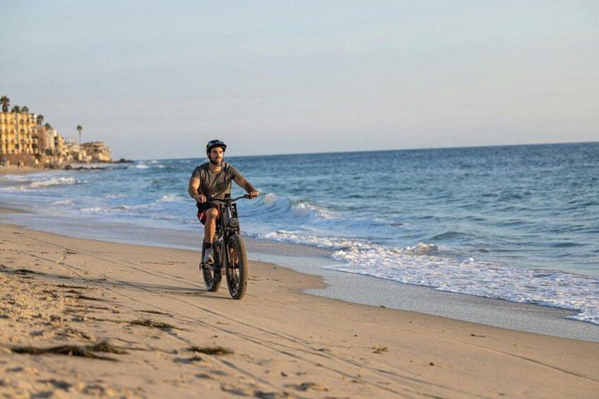Une personne à vélo sur une plage de sable, avec l’océan en arrière-plan. 3
