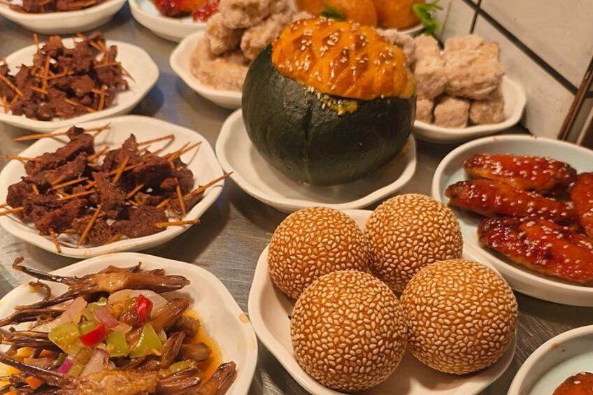 A variety of dishes including a large stuffed pumpkin, sesame balls, and other assorted foods. 5