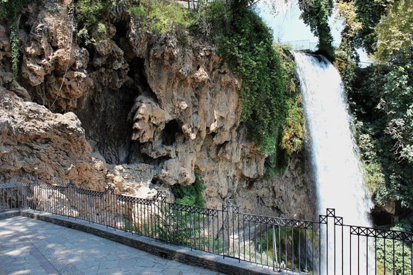 A waterfall cascading down a rocky cliff, surrounded by greenery and a metal fence. 3