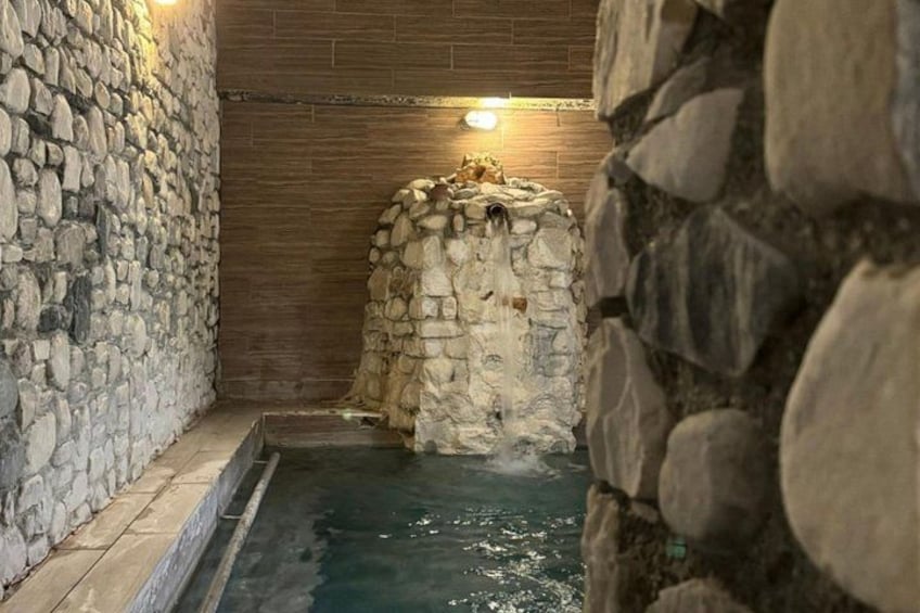A stone-walled pool with a stone archway and a wooden wall in the background. 4