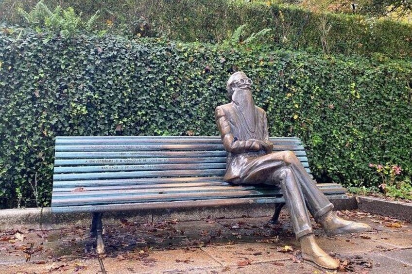 A statue of a man sitting on a bench surrounded by greenery. 4