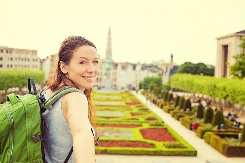 Eine Person mit grünem Rucksack, ein Garten mit geometrischen Mustern und ein Gebäude in der Ferne. 3