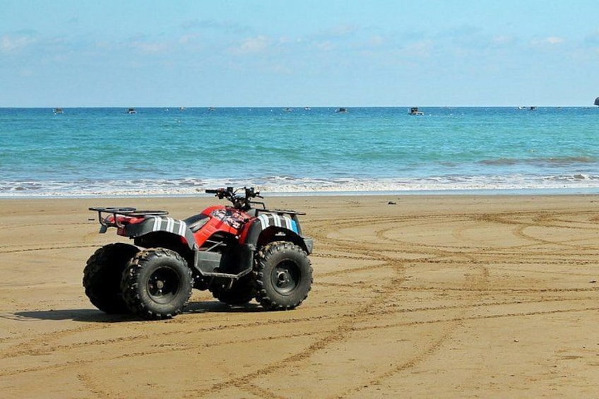 Ein rotes Geländefahrzeug am sandigen Strand, im Hintergrund das Meer. 4