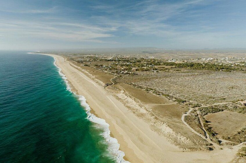 Eine Küstenlandschaft mit Sandstrand, Meereswellen und einer in der Ferne liegenden Stadtansicht. 3