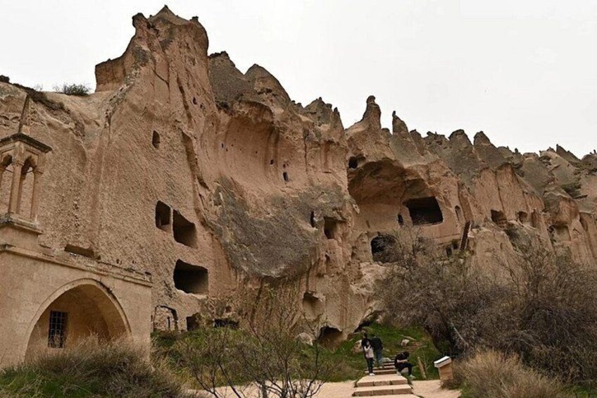 A rock formation with carved windows and an archway, surrounded by sparse vegetation. 2