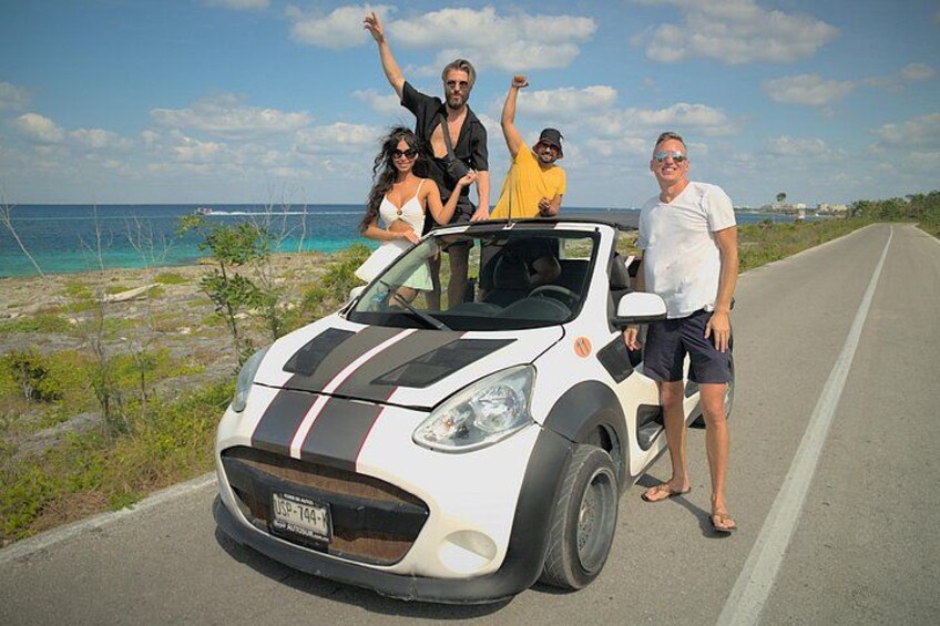 En vit bil med svarta ränder parkerad på en väg, med en strand och havet i bakgrunden. 1
