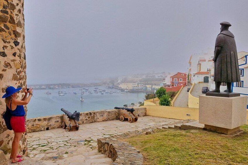 A statue, a cannon, a person taking a photo, and a coastal town. 4