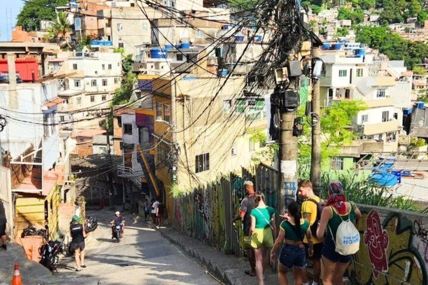 A narrow urban street with pedestrians and a motorbike, surrounded by densely packed buildings and overhead power lines. 4