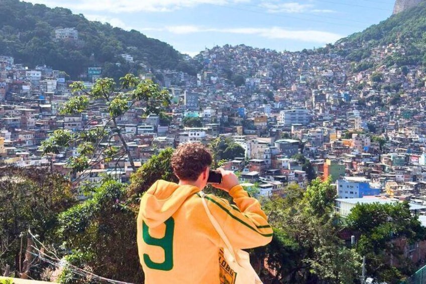 A person taking a photo of a densely packed cityscape with hills in the background. 2