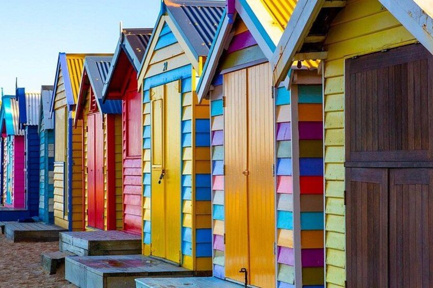Colorful wooden beach huts with sloped roofs and steps leading up to the entrance. 1