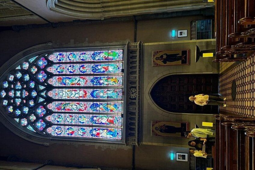 A stained glass window with intricate designs, a large arched doorway, and a person standing in the aisle. 4