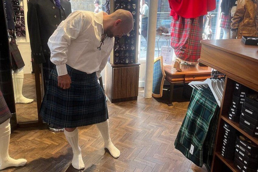 A person in a white shirt and kilt inside a store with wooden flooring and clothing racks. 3