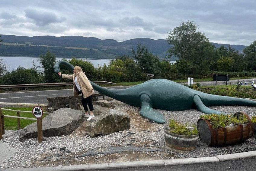 A large dinosaur sculpture by a lake with mountains in the background. 1