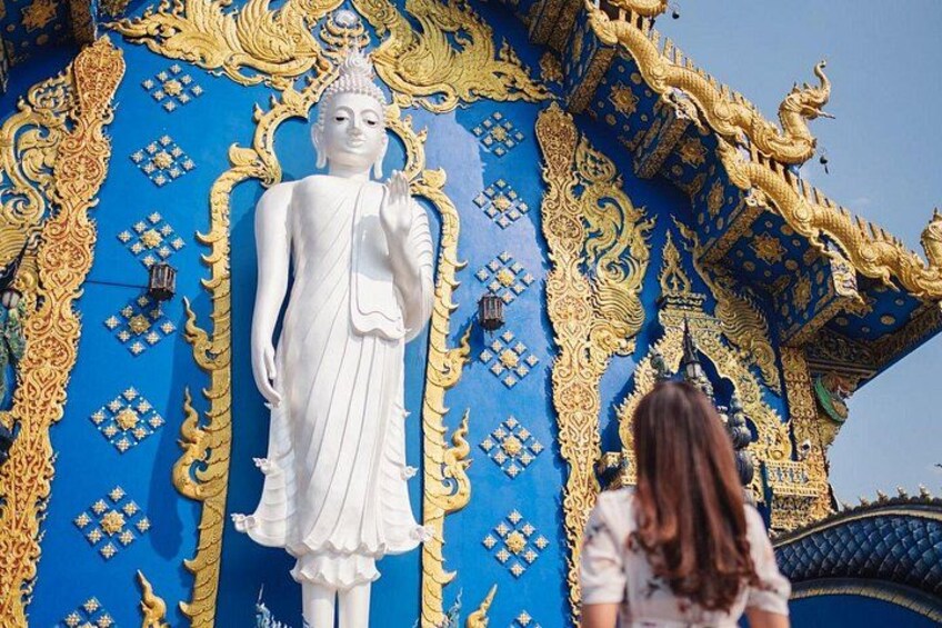 A large white statue of a figure in traditional attire, set against a blue background with golden patterns and designs. 3