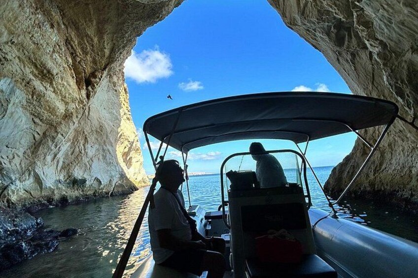 Un bote con dos personas, la entrada a una cueva rocosa y un cielo despejado. 3