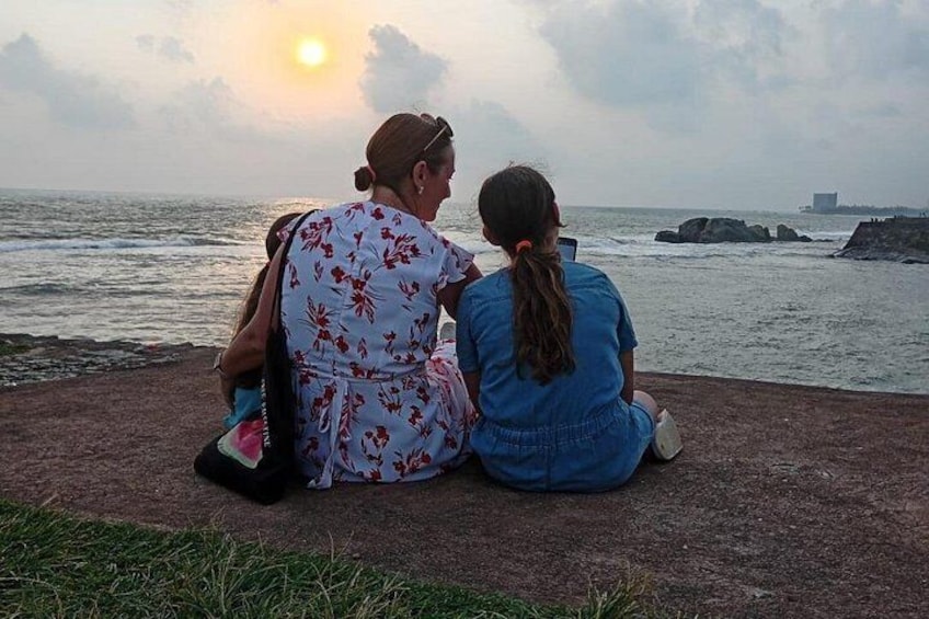 Two people sitting on a concrete ledge overlooking the ocean at sunset. 2
