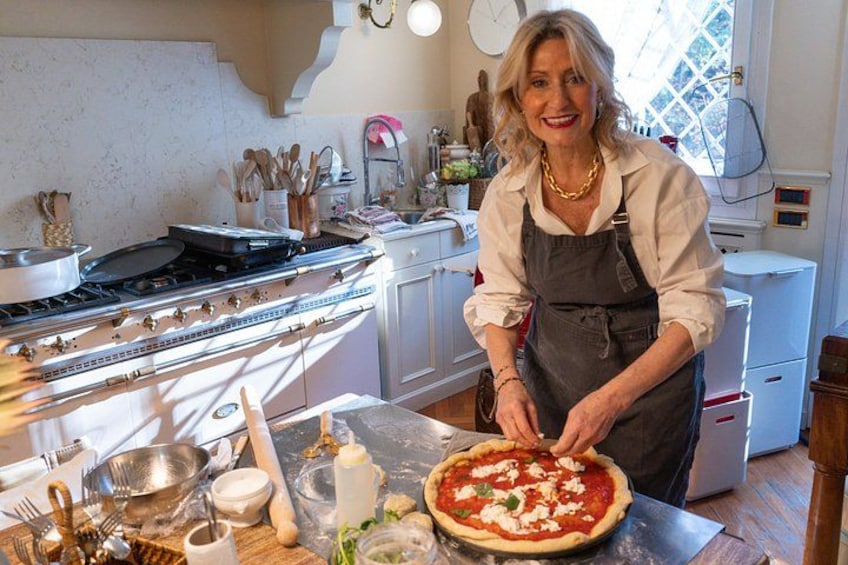 A person preparing a pizza in a kitchen with a stove, utensils, and a window. 1