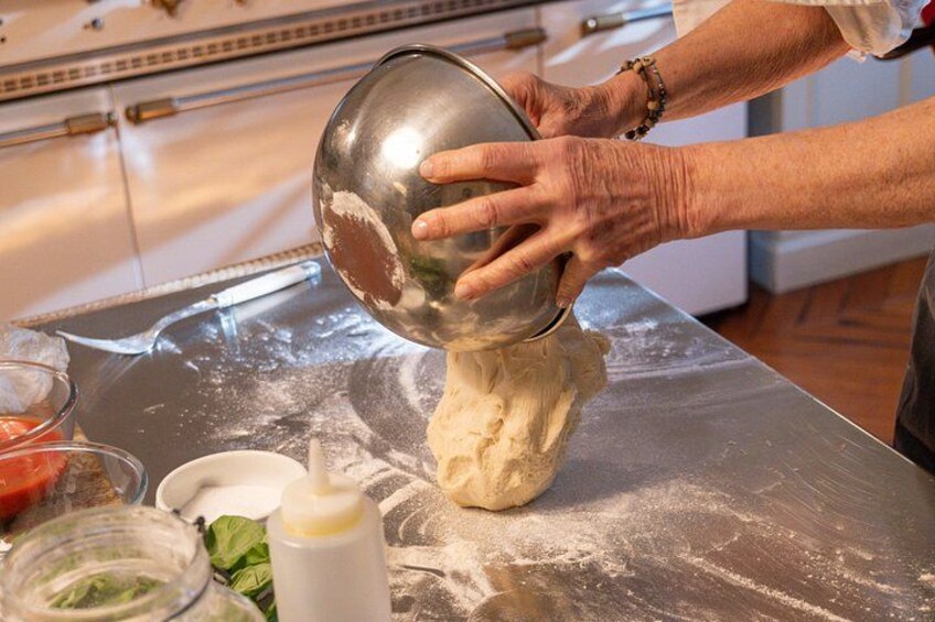 A person kneading dough on a floured surface with a bowl and a bottle of liquid nearby. 4