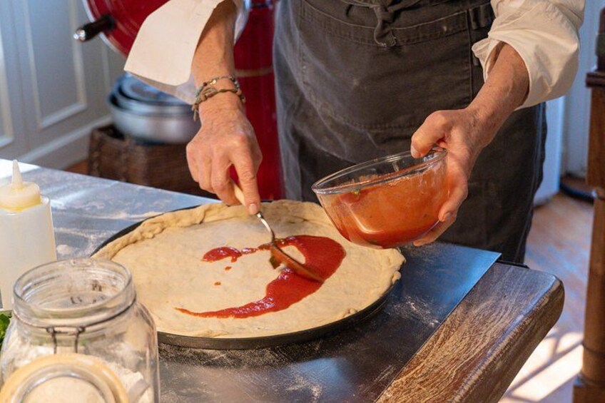 A person preparing a pie crust with tomato sauce. 2