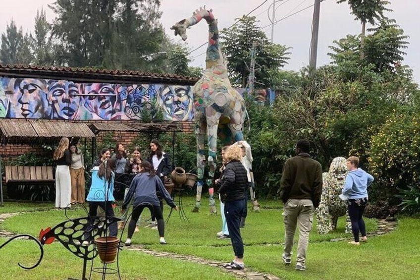 Un groupe de personnes se tient autour d’une statue de girafe dans un parc, avec une fresque murale en arrière-plan. 1
