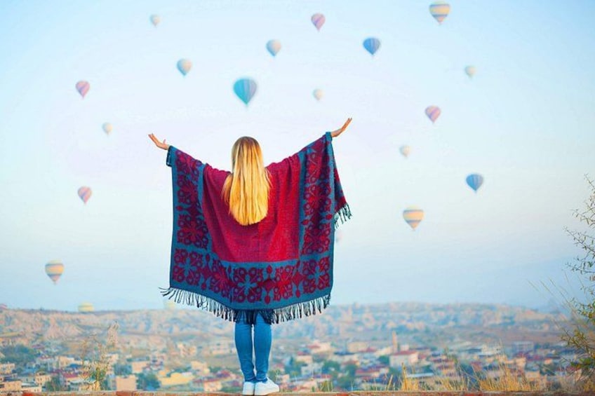 A person standing with arms outstretched, a patterned shawl, and hot air balloons in the background. 5