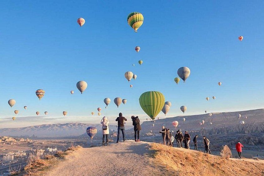 A group of people observing hot air balloons on a clear day. 2