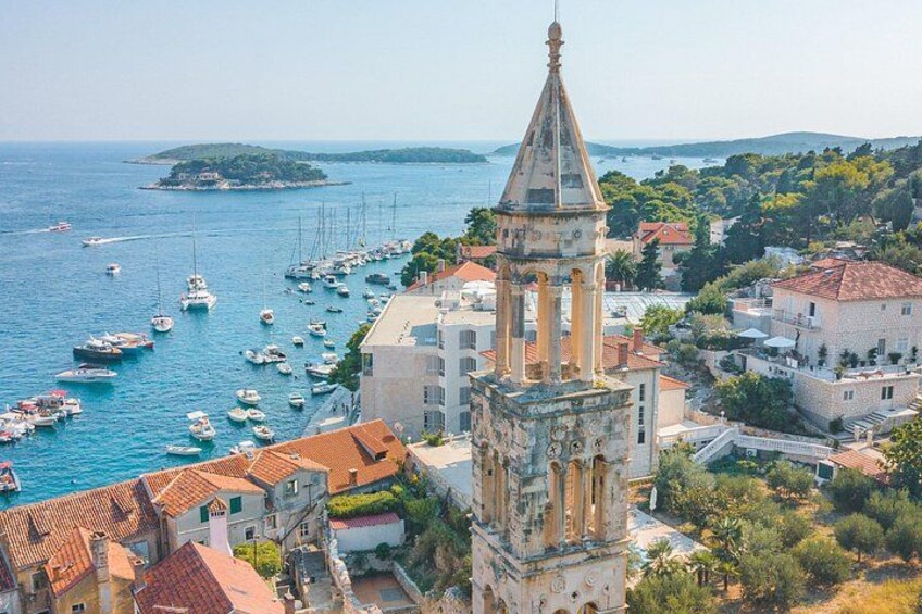 A coastal town with a prominent tower, boats in the harbor, and a distant island. 2