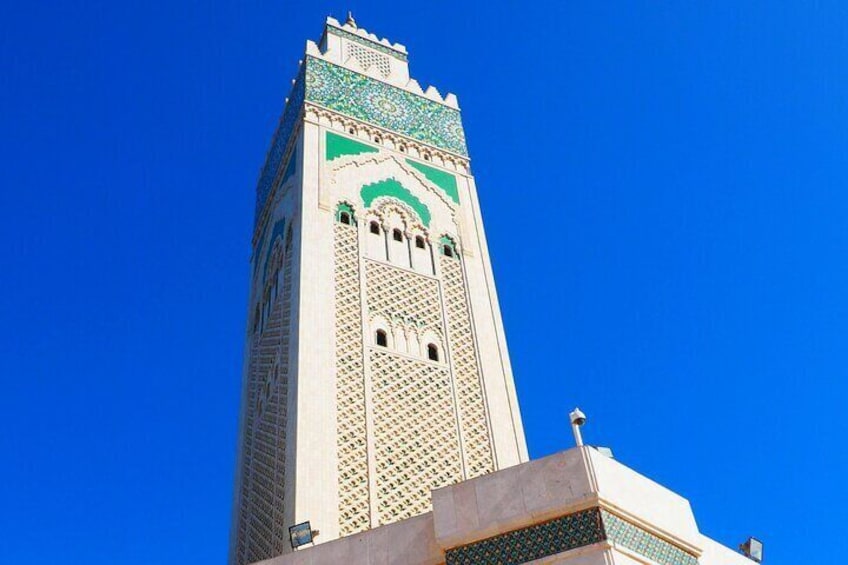 A tall minaret with intricate geometric patterns and a green-tiled top against a clear blue sky. 5