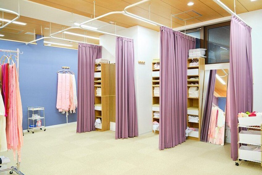 Een kamer met paarse gordijnen, planken met opgevouwen kleding, en een karretje met spullen. 3