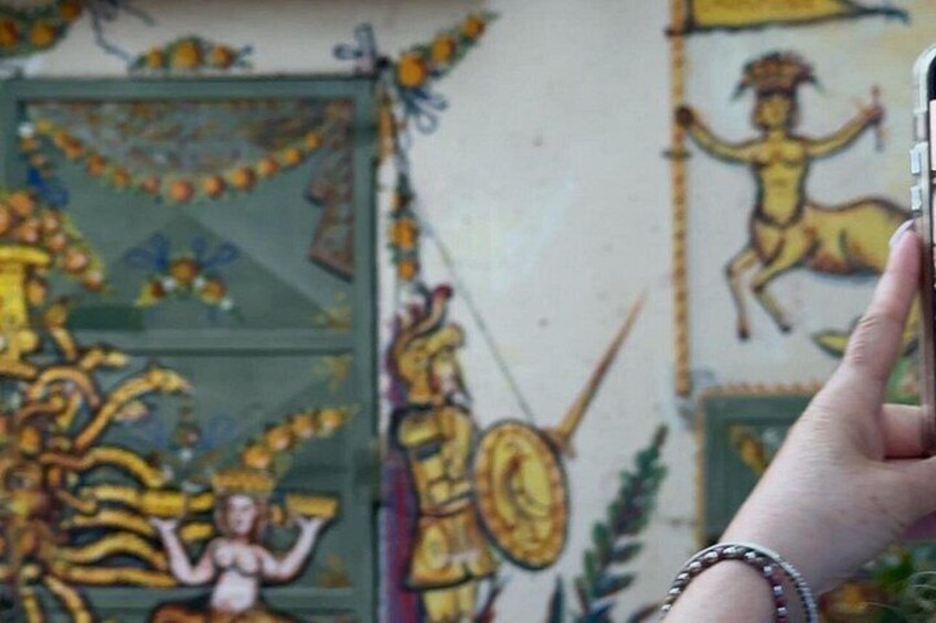 A hand holding a smartphone, capturing a mural with mythological figures and a green door. 4
