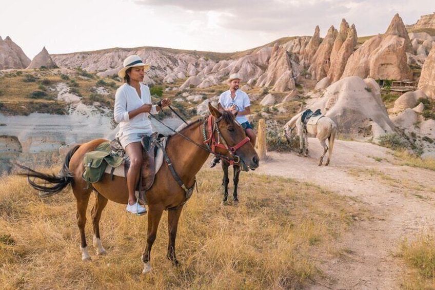Zwei Personen reiten auf Pferden einen Feldweg entlang, im Hintergrund eine felsige Landschaft. 1
