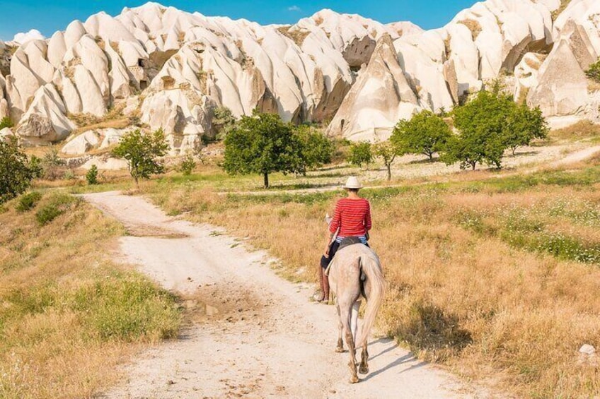 Eine Person reitet auf einem Pferd auf einem Feldweg, im Hintergrund weiße Felsformationen. 2