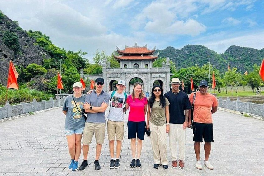 A group of people standing in front of a traditional building with a tiled roof, surrounded by greenery and flags. 4