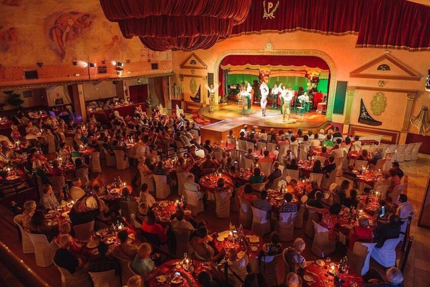 A banquet hall with round tables, a stage with performers, and a crowd of attendees. 1