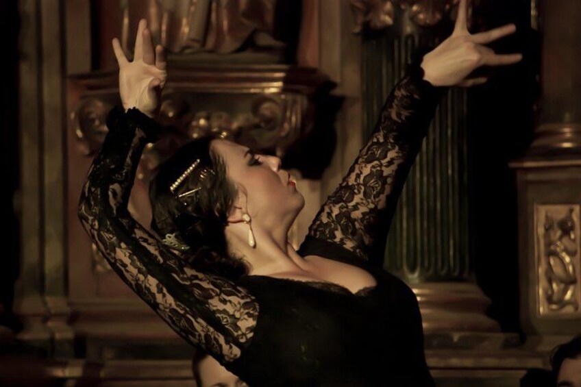 A person in a black dress with lace sleeves performing a dance in an ornate room with classical architecture. 5